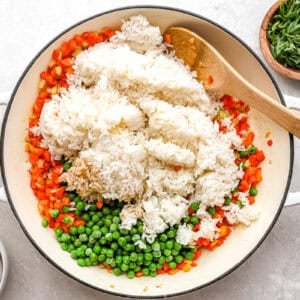 cooked rice and peas added to diced veggies in a pan with a wooden spoon.