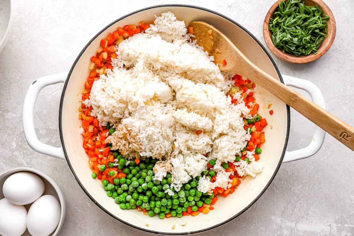 cooked rice and peas added to diced veggies in a pan with a wooden spoon.