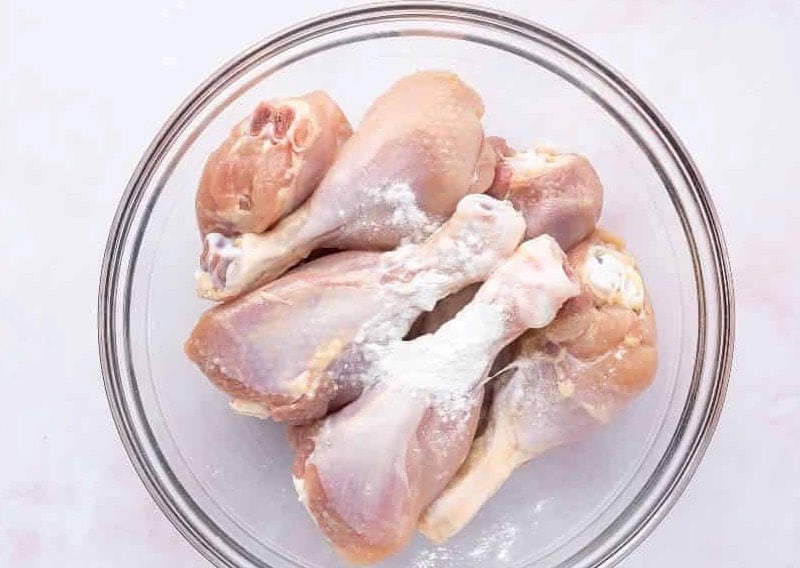 chicken drumsticks and baking powder in a glass bowl.