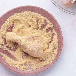 coating a chicken drumstick in seasoning on a pink plate.