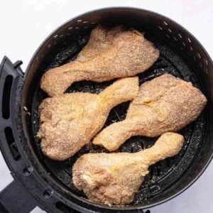 seasoned chicken drumsticks in an air fryer basket.