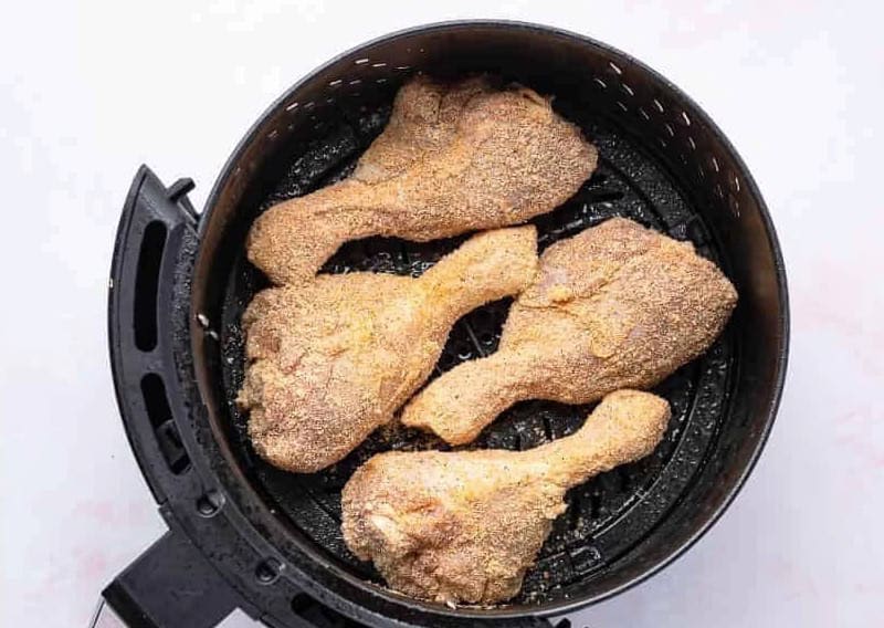 seasoned chicken drumsticks in an air fryer basket.