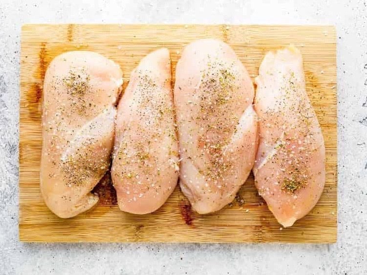 seasoned chicken breasts on a wood cutting board.