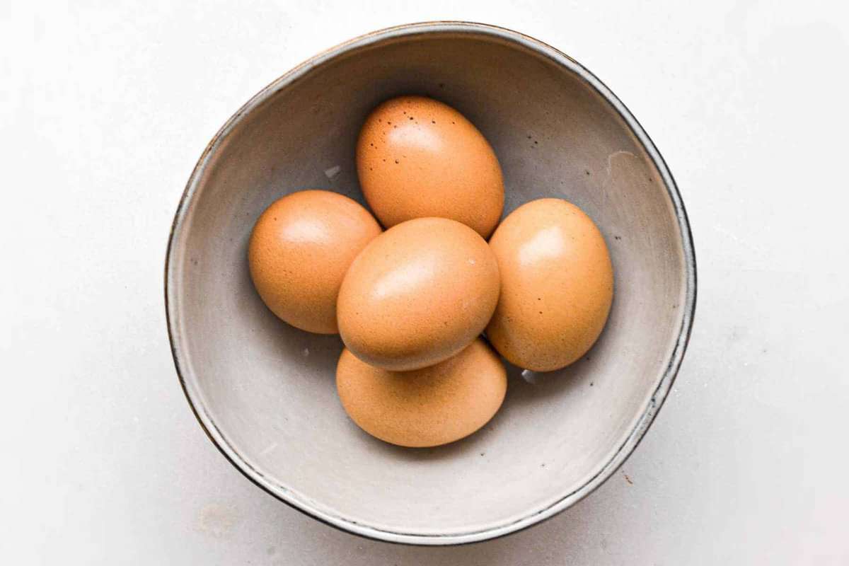 Five brown eggs cooked in an instant pot for hard boiling, beautifully presented in a bowl on a white surface.