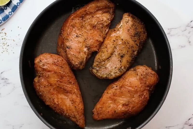 4 raw fajita seasoned chicken breasts in a skillet.
