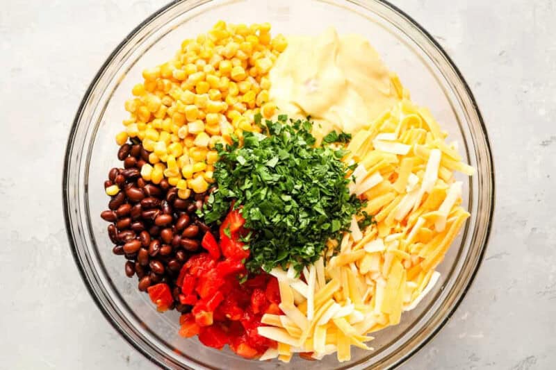 corn, beans, tomatoes, cheese, cream of chicken soup, and cilantro in a glass bowl.
