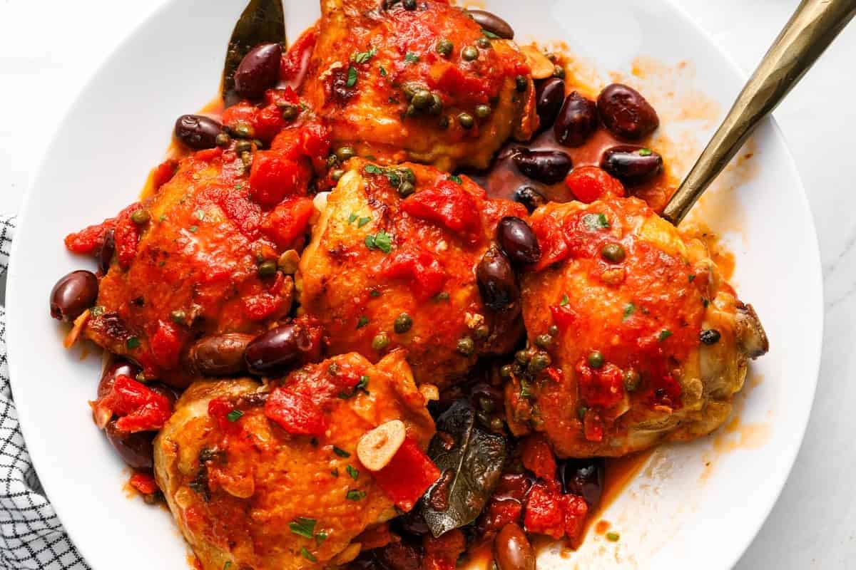 plated chicken thighs served with puttanesca sauce.