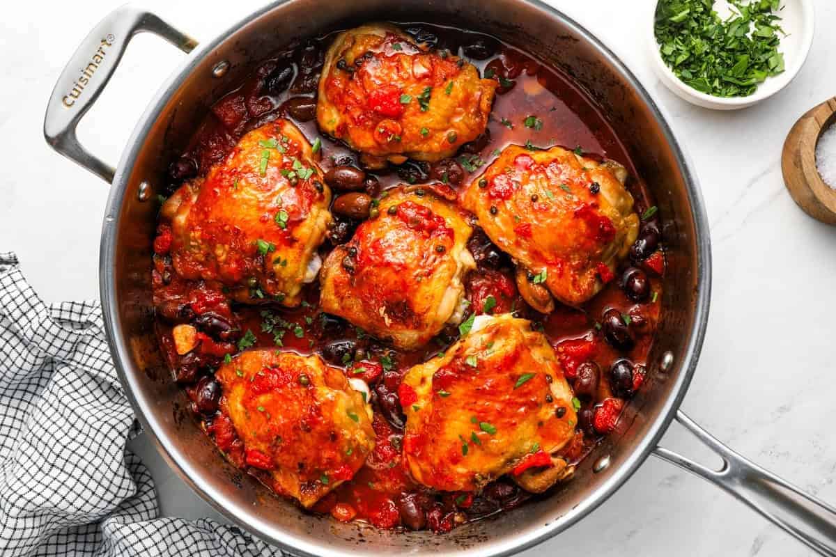 chicken puttanesca in a sauté pan topped with chopped parsley.