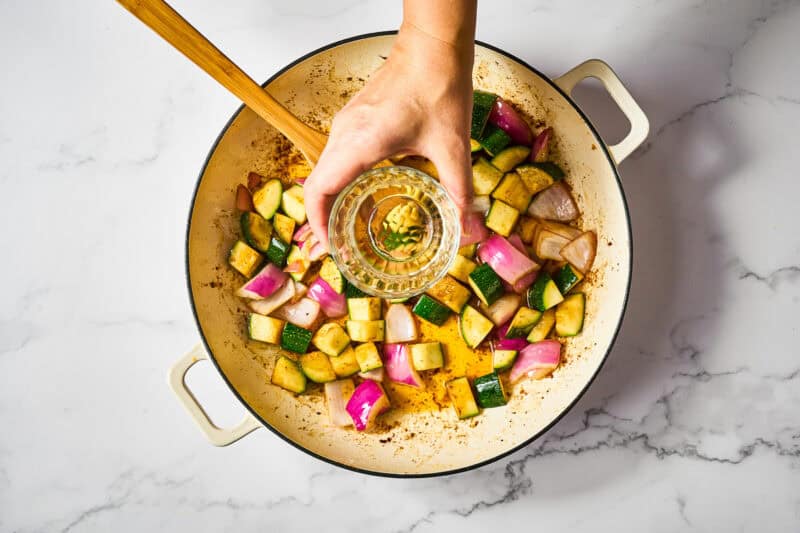 pouring white wine over sautéed veggies in a skillet.