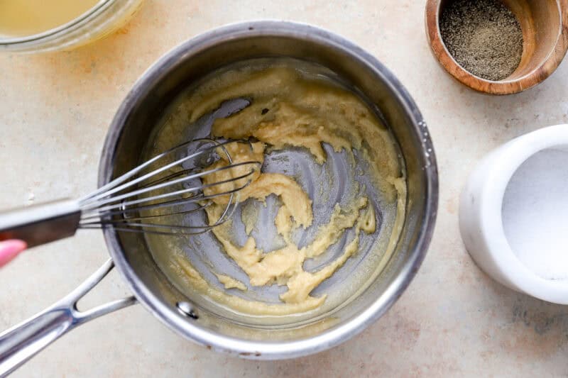 whisking a butter and flour roux in a saucepan.