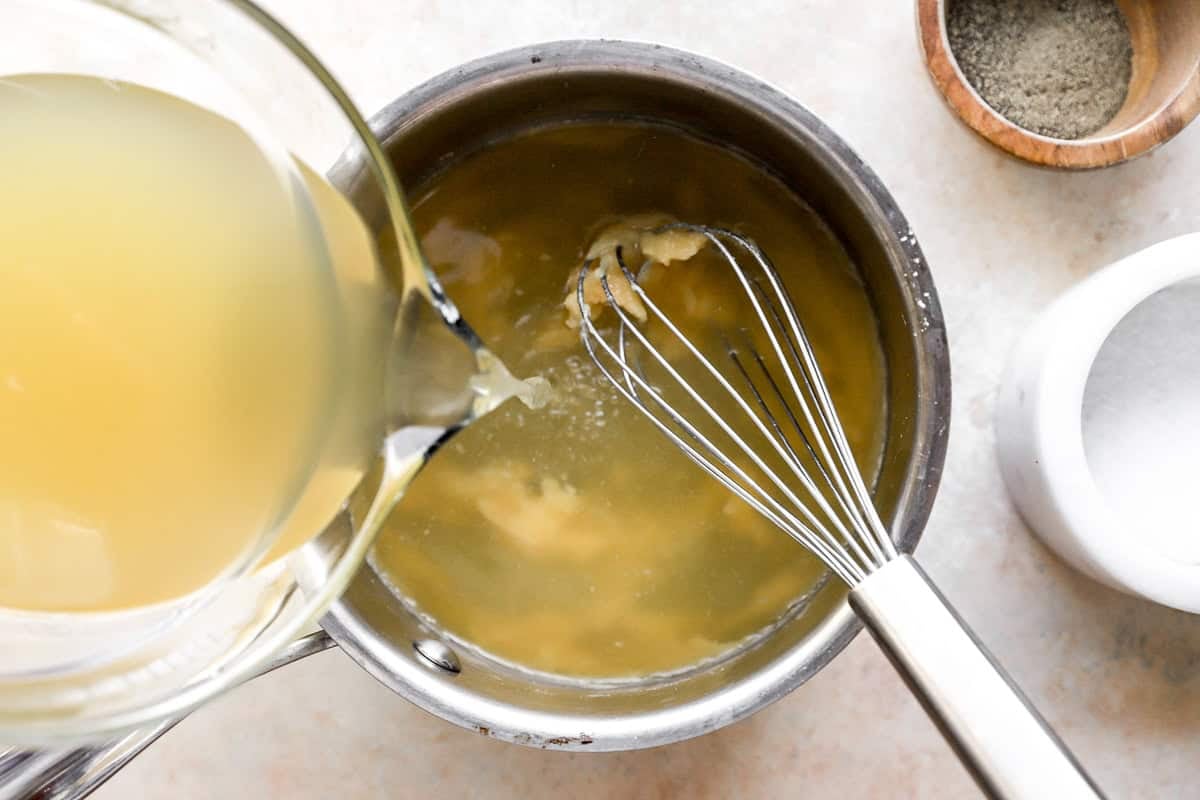 pouring chicken broth over a roux in a saucepan with a whisk.