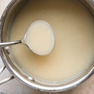 lifting a scoopful of thickened chicken gravy from a saucepan.