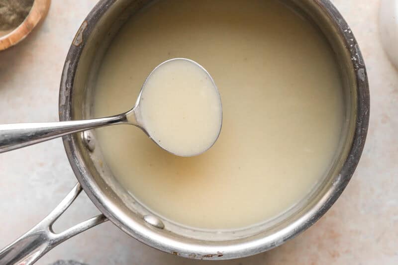 lifting a scoopful of thickened chicken gravy from a saucepan.