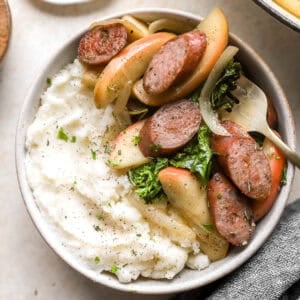 a serving of apple chicken sausage skillet in a bowl with mashed potatoes.