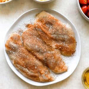 seasoned raw chicken breasts on a white plate.