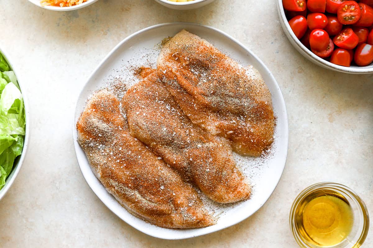seasoned raw chicken breasts on a white plate.