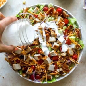 pouring ranch dressing over chopped chicken salad in a large bowl.