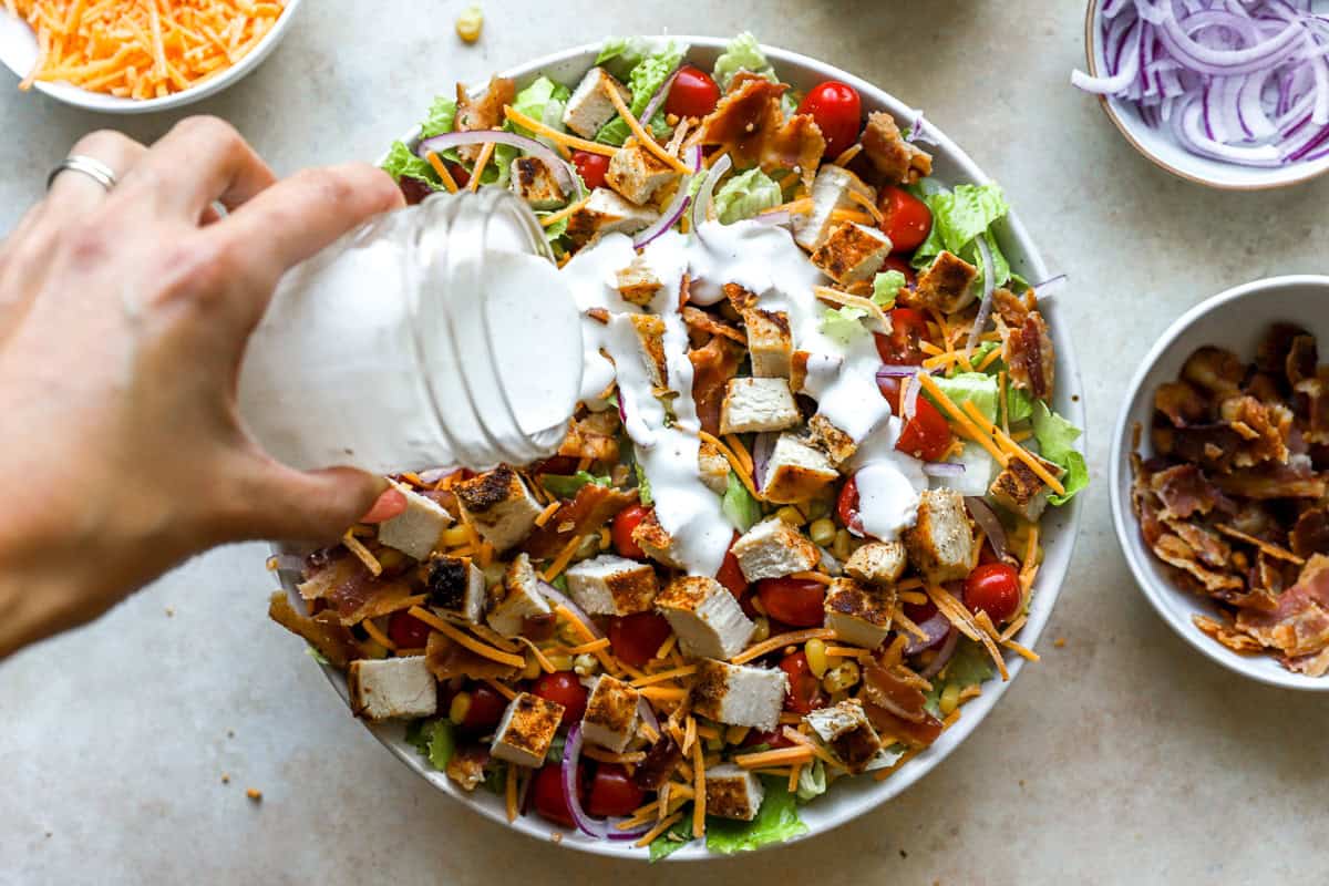 pouring ranch dressing over chopped chicken salad in a large bowl.