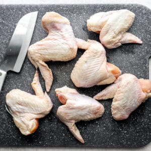 6 whole raw chicken wings on a cutting board with a sharp knife.