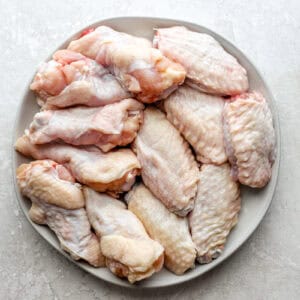 raw separated chicken wing pieces on a white plate.