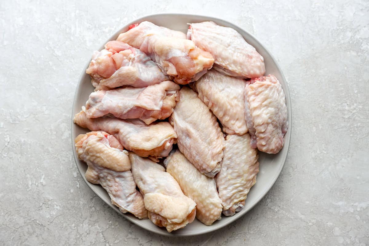 raw separated chicken wing pieces on a white plate.