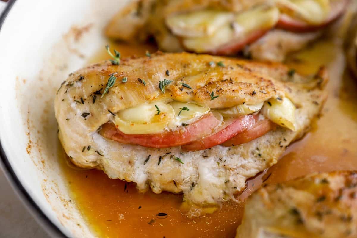 closeup view of a seasoned chicken breast stuffed with apples and brie in a pan.