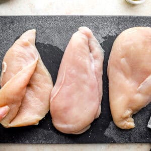 opening a pocket in a raw chicken breast on a cutting board.