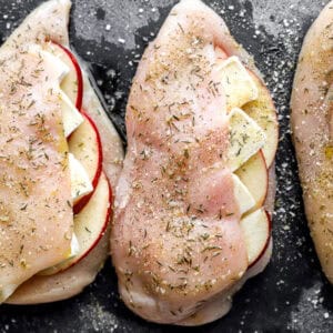 closeup of seasoned apple brie stuffed raw chicken breasts on a cutting board.