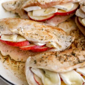 closeup of seared apple brie stuffed chicken breasts in a pan.