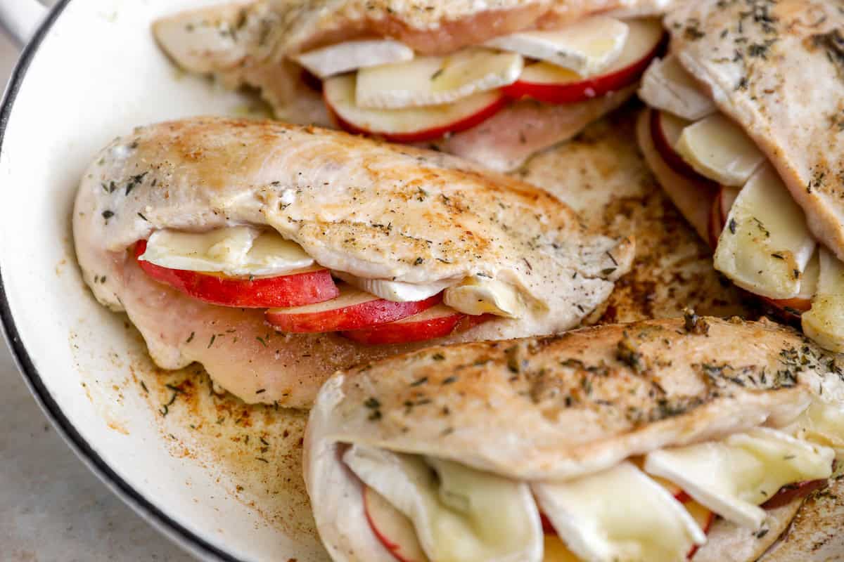 closeup of seared apple brie stuffed chicken breasts in a pan.