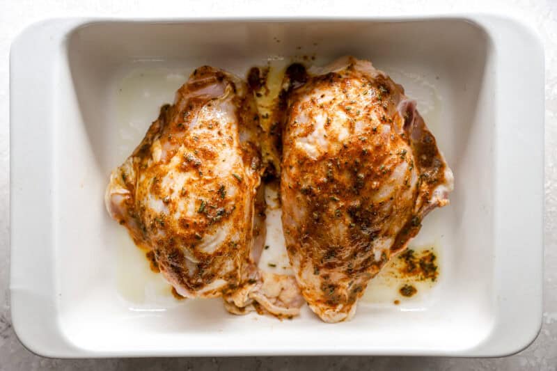 seasoned raw split chicken breasts in a baking dish.