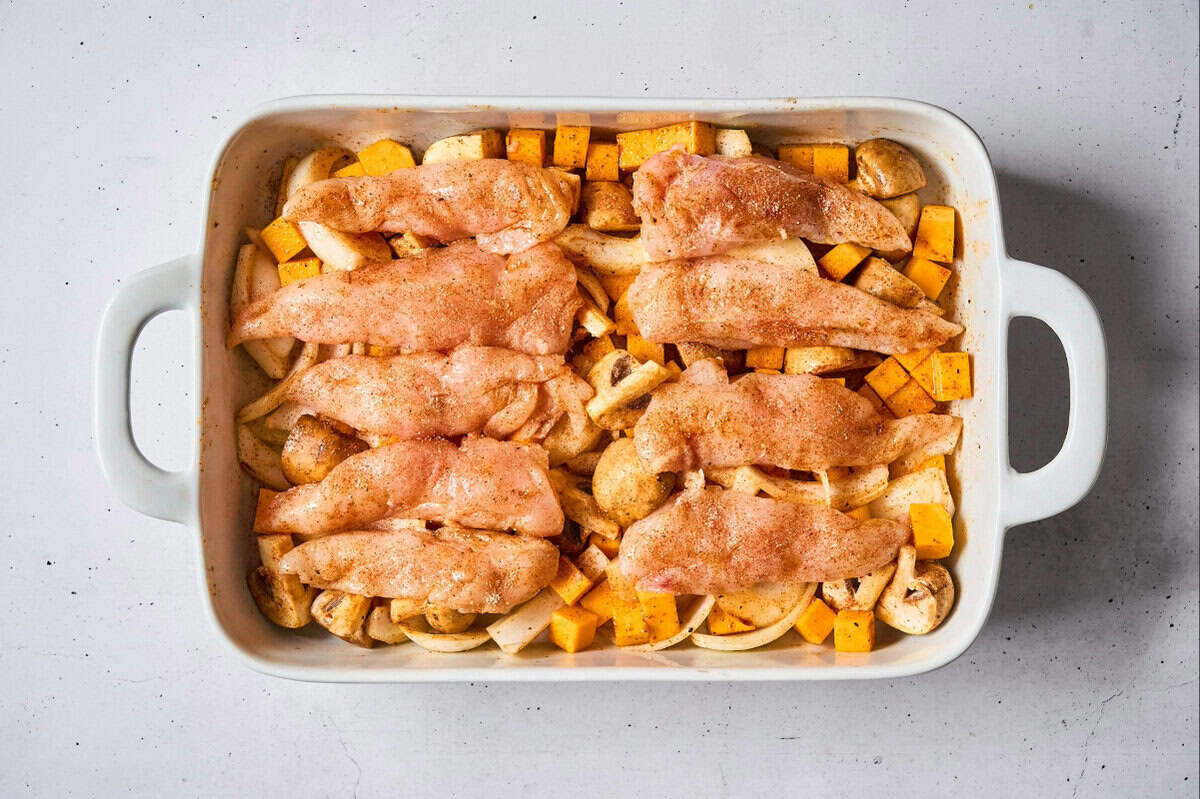 seasoned raw chicken tenders draped over seasoned veggies in a baking dish.