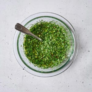 chimichurri sauce in a glass bowl with a spoon.