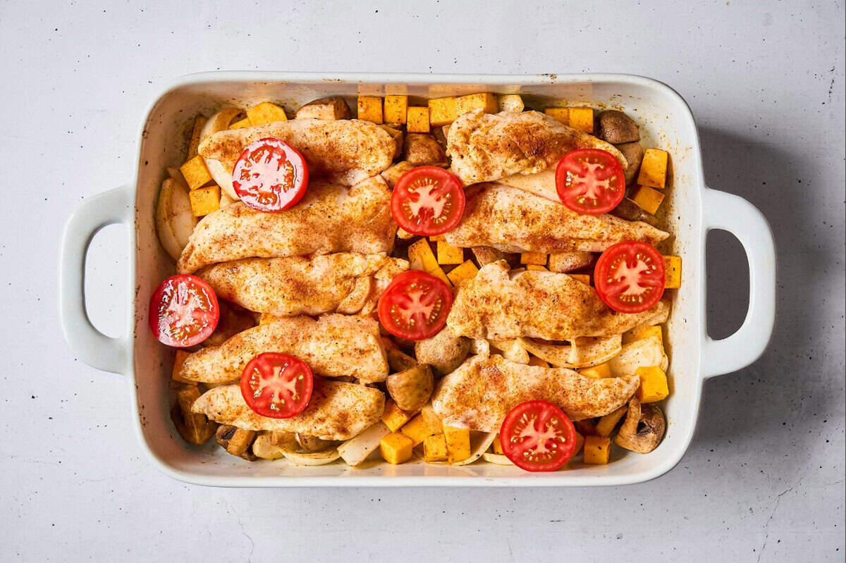 partially cooked chicken tenders and veggies topped with tomato halves in a baking dish.