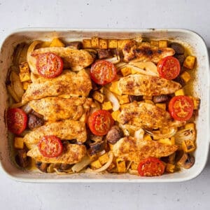 cooked chicken tenders and veggies topped with tomato halves in a baking dish.
