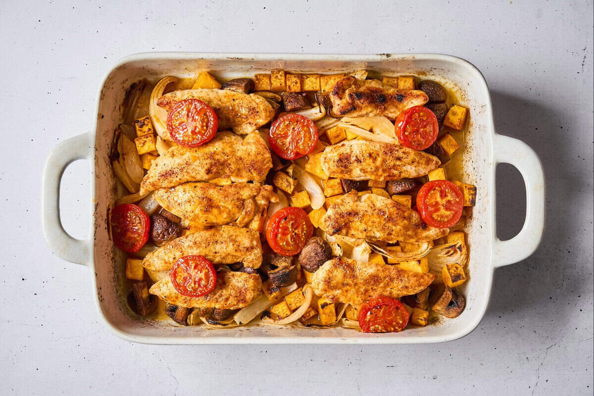 cooked chicken tenders and veggies topped with tomato halves in a baking dish.