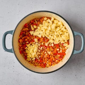 adding ginger, garlic, and apple to sautéed diced vegetables in a dutch oven.