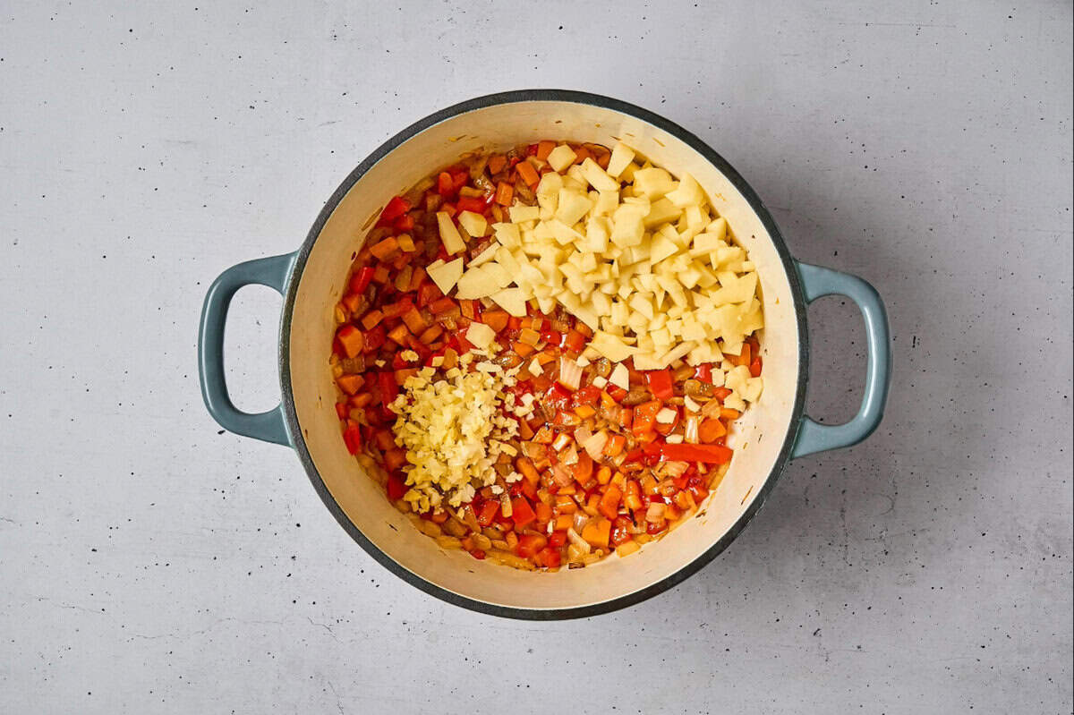 adding ginger, garlic, and apple to sautéed diced vegetables in a dutch oven.