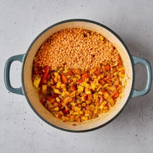 adding dried red lentils to sautéed spiced vegetables in a dutch oven.