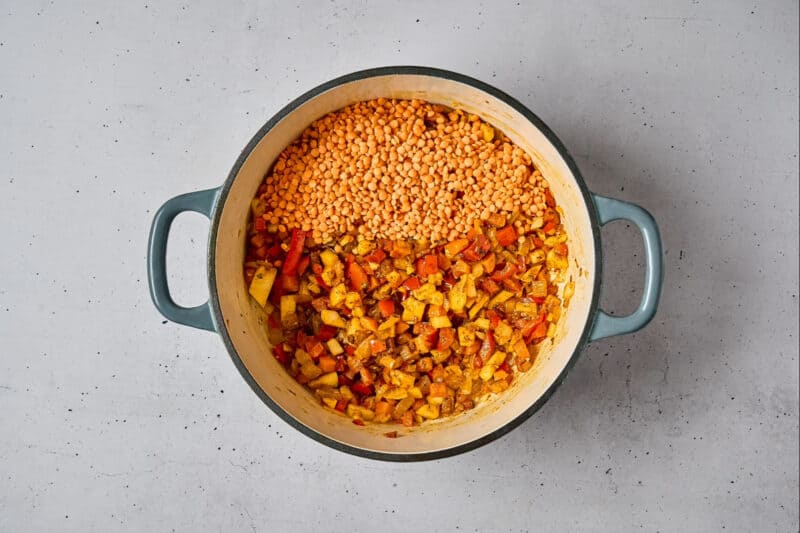 adding dried red lentils to sautéed spiced vegetables in a dutch oven.
