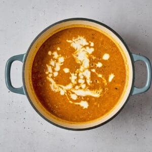 adding coconut milk to mulligatawny soup in a dutch oven.