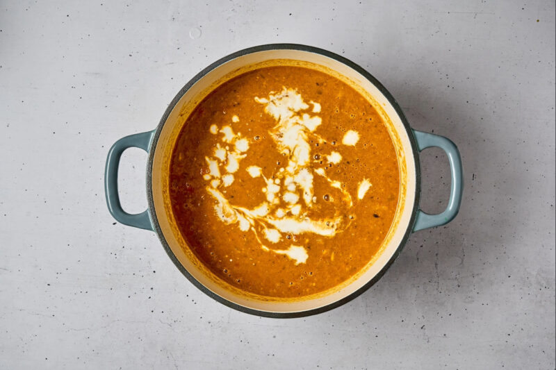 adding coconut milk to mulligatawny soup in a dutch oven.
