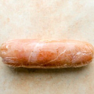 a rolled seasoned chicken breast wrapped tightly in plastic wrap.
