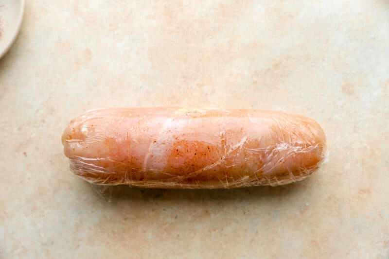 a rolled seasoned chicken breast wrapped tightly in plastic wrap.