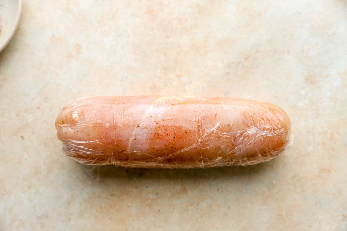 a rolled seasoned chicken breast wrapped tightly in plastic wrap.
