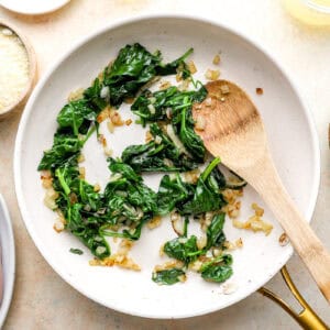 sautéed onions and spinach in a frying pan with a wooden spoon.