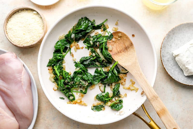 sautéed onions and spinach in a frying pan with a wooden spoon.