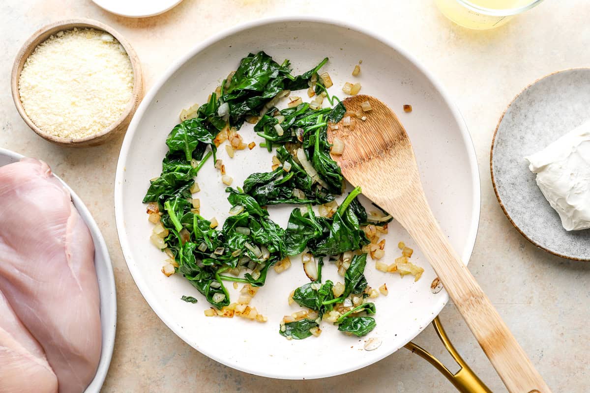 sautéed onions and spinach in a frying pan with a wooden spoon.
