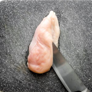 slicing a raw chicken breast lengthwise.