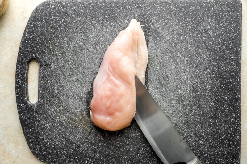 slicing a raw chicken breast lengthwise.